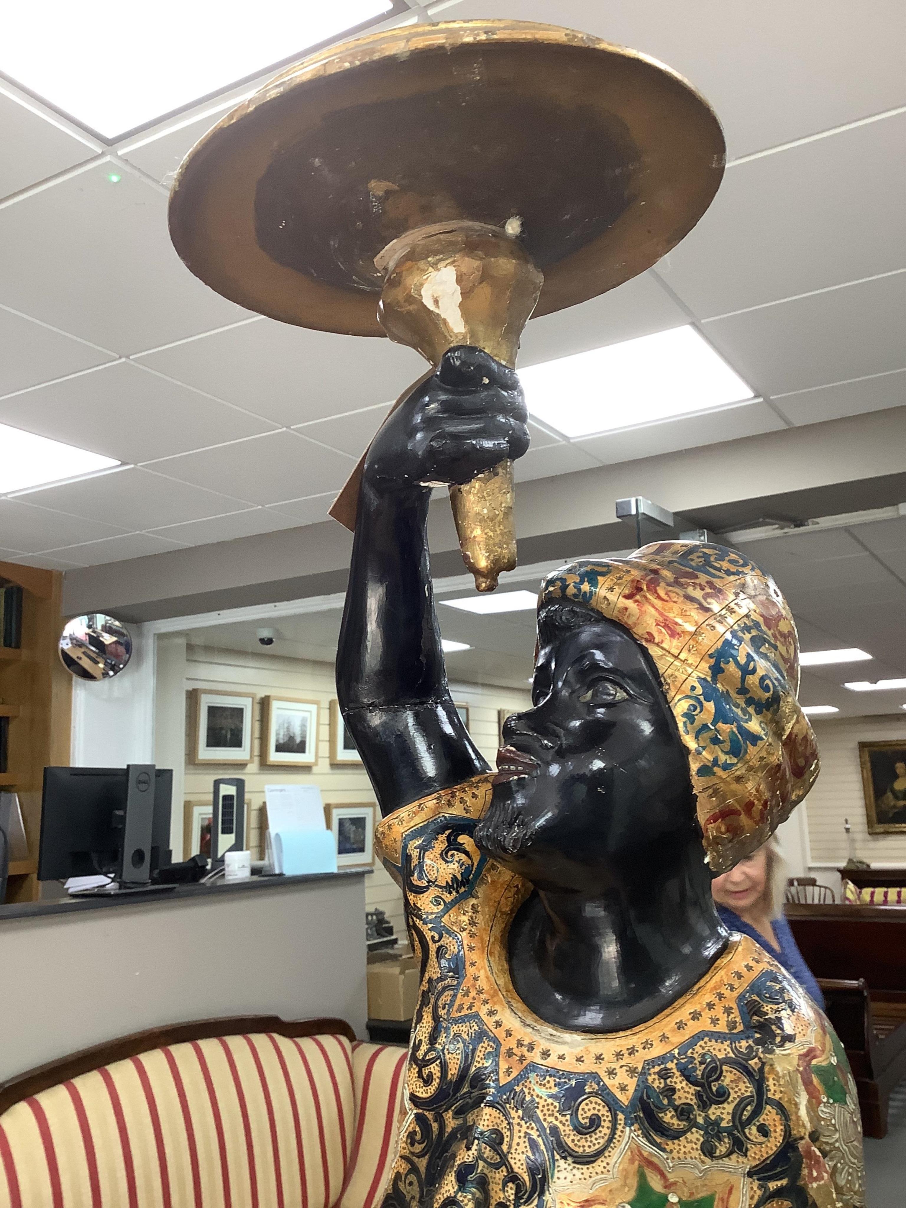 A 19th century Italian carved wood and composition polychrome painted blackamoor torchere, modelled standing with one arm holding a scroll pillar on waisted circular base and lions paw feet, 106cm high